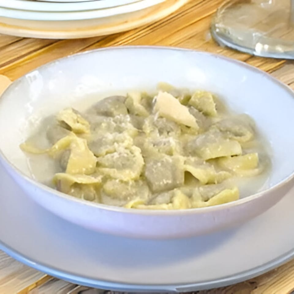 A white bowl filled with Nonna Dora's Italian tortellini in a creamy sauce, topped with shaved parmesan.