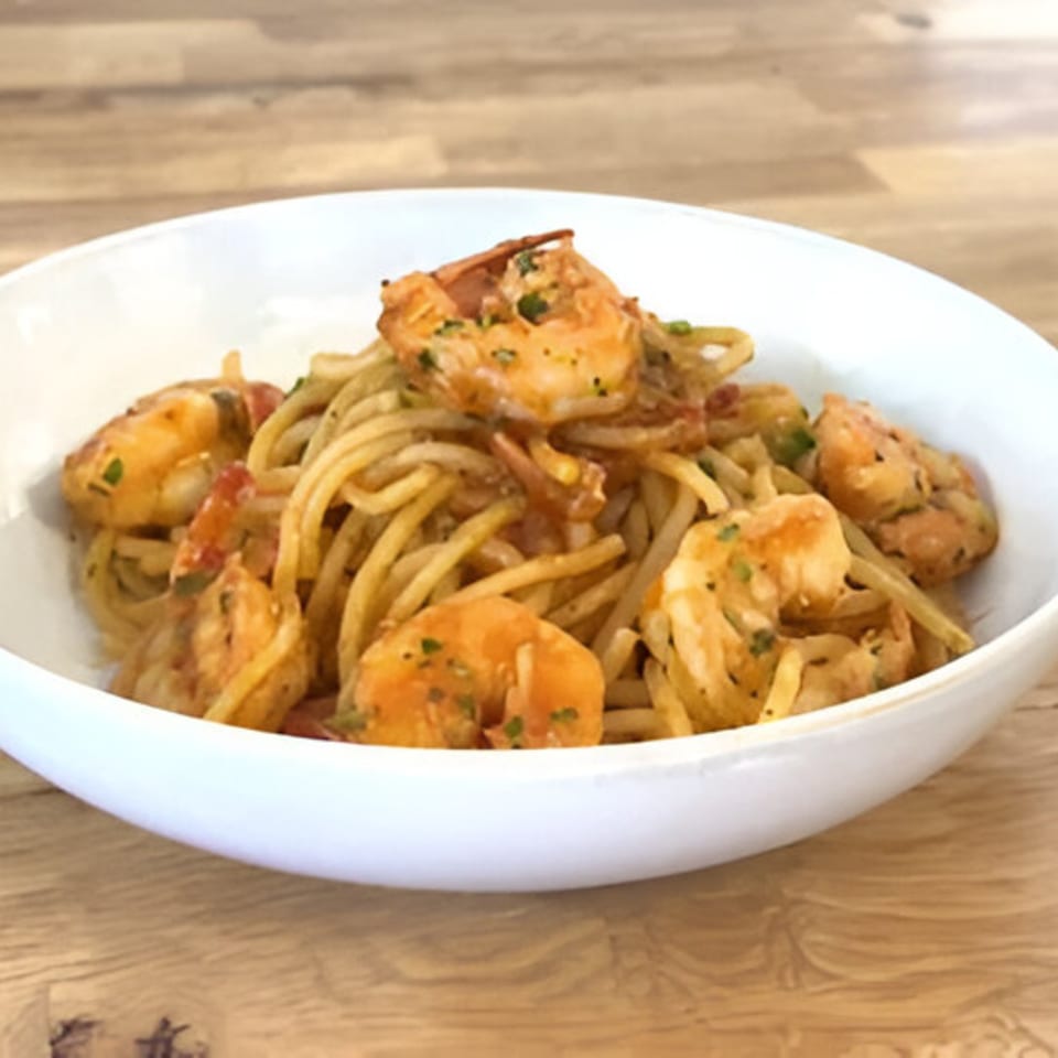 A white bowl filled with Nonna Dora's shrimp scampi pasta, featuring spaghetti and large shrimp.