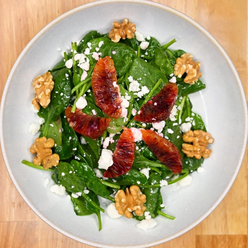Spinach salad with blood orange segments, walnuts, and crumbled feta cheese in a white bowl.