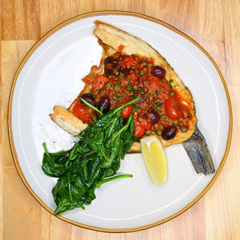 Nonna Dora Italian Eatery's baked fish with tomato sauce, olives, capers, spinach, and a lemon wedge.